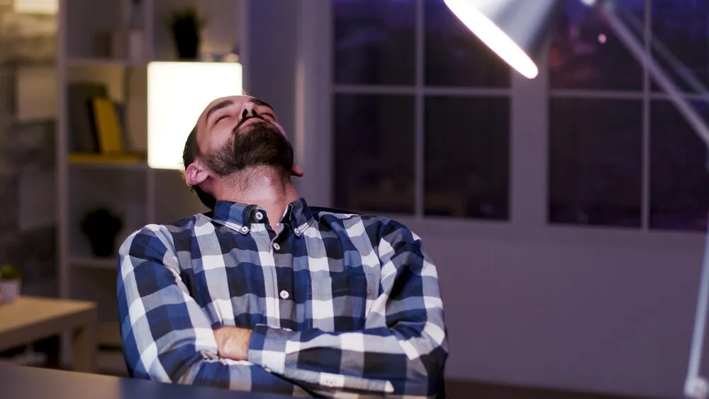 jovem empreendedor caucasiano cansado dormindo na cadeira em seu home office. empresário sobrecarregado.