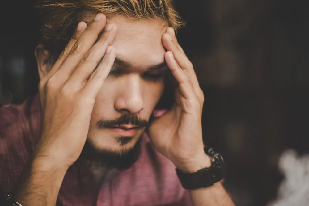 jovem hipster com a mão na cabeça olha seriamente enquanto pensa sentado em um café.