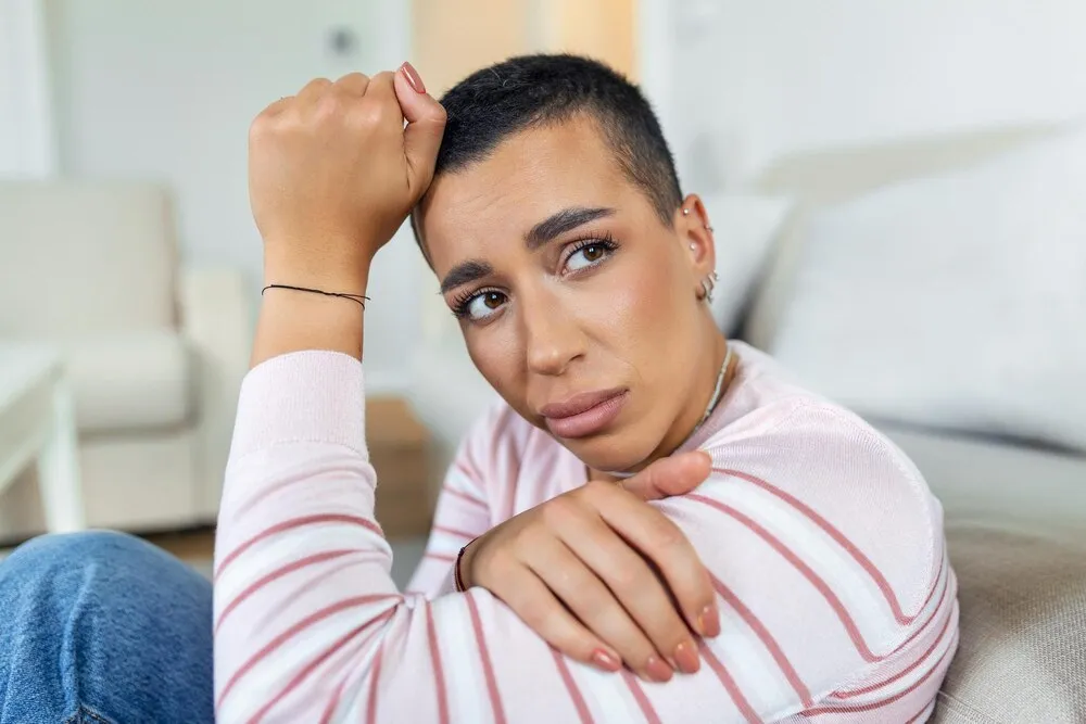 mulher afro-americana infeliz no sofá chorando mulher triste solitária imersa em pensamentos sentada sonhando acordada ou esperando por alguém na sala de estar com uma expressão séria sentada no sofá