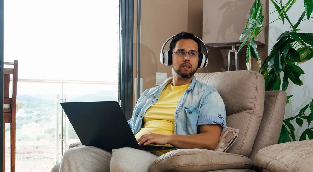 Foto horizontal de um homem ouvindo música com fones de ouvido e notebook no colo