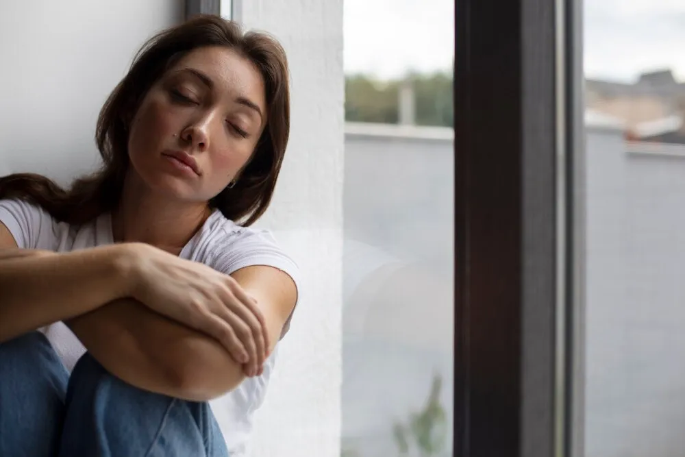 retrato de uma mulher jovem com baixa autoestima sentada perto da janela em casa