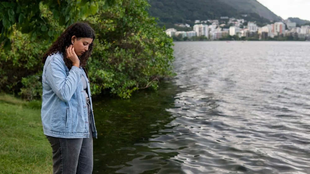 mulher triste e contemplativa sentada à beira do lago