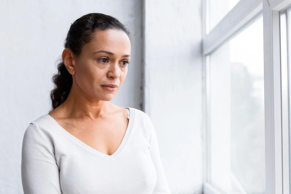 mulher triste olhando pela janela para uma sessão de terapia de grupo